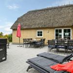 Terrasse mit Liegen, Tischen und Stühlen vor einem Haus mit Strohdach.