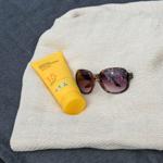 Sonnencreme und Sonnenbrille auf einem weißen Tuch.