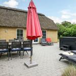Terrasse mit Tisch, Stühlen, Sonnenschirm und Whirlpool. Hintergrund: Haus mit Strohdach.