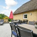 Terrasse mit Tisch, Stühlen und Liegestühlen vor einem Haus mit Strohdach.