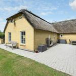 Haus mit Strohdach, Terrasse, Garten und Sitzgelegenheiten.