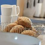 Küchenarbeitsplatte mit Korb voller Brötchen und weißen Tassen.