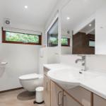 Bathroom with sink, mirror, toilet, and window with view of greenery.