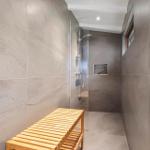Shower area with glass enclosure, wooden bench, and wall niche. Floor and walls are tiled with stone.