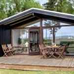 Modern cabin with wooden deck and large glass area. Furniture and table are outside.