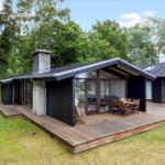 Modern villa with wooden terrace and garden. Large glass front, seating areas, and barbecue space.