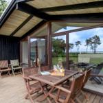 Deck with wooden table and chairs, large glass walls, view of lawn and trees.