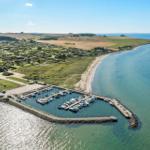 Marina with boats along coast, beach, and green landscape in background.