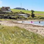 Beach with people, houses, and green hills in the background.