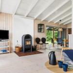 Living room with fireplace, TV, and dining area. Wooden floors and white ceiling beams.