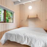 Bedroom with wood walls, bed, and window view of forest.