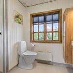 Badezimmer mit Toilette, Waschbecken und Dusche. Holzfenster und Wandpaneelen.