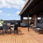 Terrasse mit Sitzgruppe, Esstisch und Kaminofen. Holzdecke und Blick auf die Umgebung.