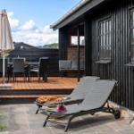 Terrasse mit Liegestühlen, Tisch und Stühlen neben einem schwarz gestrichenen Haus.