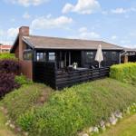 Schwarzes Holzhaus mit Terrasse, Garten und Blick auf Wasser.