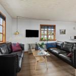 Wohnzimmer mit zwei schwarzen Ledersofas, Holztisch und Fenstern mit Holzrahmen.
