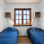 Zwei Betten mit blauen Bettdecken, Fenster mit Blick aufs Meer, Holzwand und Schränke.