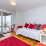 Schlafzimmer mit Blick aufs Meer, rote Polster und Teppich, weiße Wand und Holzboden.