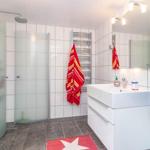 Badezimmer mit Dusche, Waschbecken und Handtüchern an Wänden.