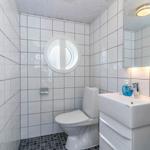 Badezimmer mit Toilette, Waschbecken und runden Fenster. Fliesenwand und Spiegel.