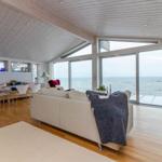 Wohnbereich mit Küchenzeile, Sofa und Blick aufs Meer durch große Fenster.