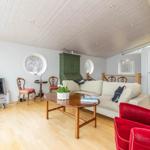 Wohnzimmer mit Sofa, rotem Sessel, Holztisch und Rundfenstern.