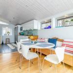 Essbereich mit Tisch, Stühlen und Sofa. Küche im Hintergrund. Holzboden und weiße Wände.