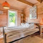 Bedroom with wooden walls, bed, nightstand, and door to the garden.