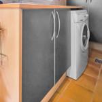 Washing machine next to kitchen cabinets with wooden top and metal rack.