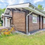 Wooden house with terrace, bicycle, and lawn. Windows and roof details visible.