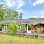 Wooden house with terrace, garden, and view of trees under blue sky.