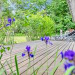 Wooden terrace with lounge chairs and blooming flowers in the green.