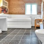 Bathroom with bathtub, toilet, and sink. Wooden walls and tiled floor.