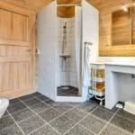 Bath with shower, sink, and toilet. Wooden walls and tiled floor.