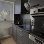 Küche mit Dunstabzug, Herd und Spüle. Fenster mit Blumenvase und Heizkörper.