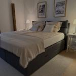 Schlafzimmer mit Bett, Nachttischen und Wandbildern.