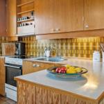 Küche mit Holzschränken, Mosaikwand und Obstschale auf Arbeitsplatte.