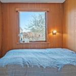 Schlafzimmer mit Holzwänden, Bett und Fenster mit Blick auf Bäume.
