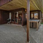 Terrasse mit Grill und Esstisch unter Holzüberdachung. Blick ins Haus durch Glastüren.