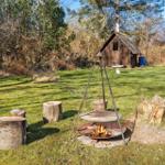 Feuerstelle mit Grill und Holzstümpfen auf Grünfläche vor Holzschuppen