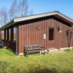 Holzhaus mit Eingangstür, Bank und Garten. Bäume im Hintergrund.