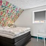 Schlafzimmer mit Bett, Stuhl und floraler Wandtapete. Fenster mit Rollladen.