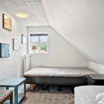 Zimmer mit Bett, Stuhl und Wandbildern unter schrägem Dach
