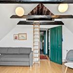 Wohnzimmer mit grafer Sofa, Holzboden und Leiter zur Dachbodenebene.