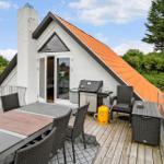 Terrasse mit Grill, Tisch und Stühlen vor einem Haus mit orangefarbenem Dach.
