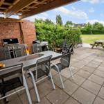 Terrasse mit Grill, Tisch und Stühlen. Im Hintergrund Grünfläche und Picknicktisch.