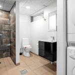 Badezimmer mit Dusche, Toilette und Waschbecken. Nebenbei steht eine Waschmaschine.