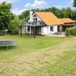 Haus mit Terrasse, Grill und Trampolin auf grünem Grundstück.