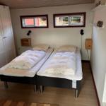 Two beds with white bedding, two windows, closet and wall shelves.