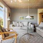 Wohnzimmer mit zwei Sofas, Glas-Tisch und Holzdecke. Große Fenster mit Blick auf Garten.